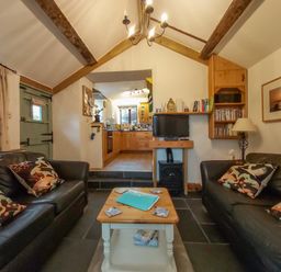 A living room with two black sofas a wooden coffee table a television and a view into a kitchen at Groom Cottage in Poughill near Bude