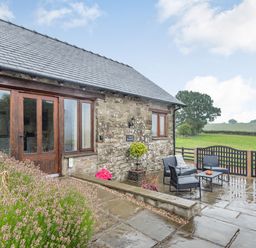 An outdoor patio with chairs and table next to a stone building with wooden doors and windows at The Granary in Llanfair Caereinion near Welshpool