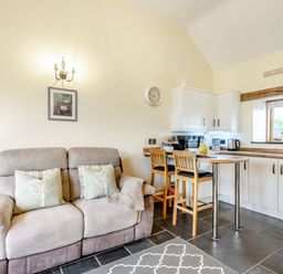 A living room with a sofa and cushions next to a kitchen with stools and cabinets at The Granary in Llanfair Caereinion near Welshpool