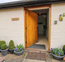 An entrance with a wooden door open revealing a kitchen inside several potted plants around the doorway on a stone and gravel ground at The Milking Parlour in Yarpole near Leominster