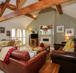 A living room with leather sofas, wooden beams, a coffee table, a dining table with chairs, and a TV at The Milking Parlour Yarpole near Leominster