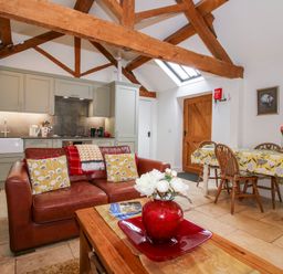 An open kitchen and dining area with wooden beams on the ceiling and a brown leather sofa at The Milking Parlour in Yarpole near Leominster