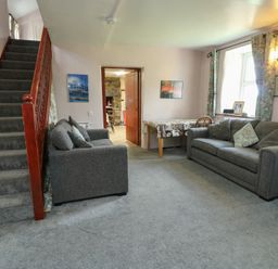 A living room with a staircase, sofas and a table at Glan y Gors in Dinorwic near Llanberis