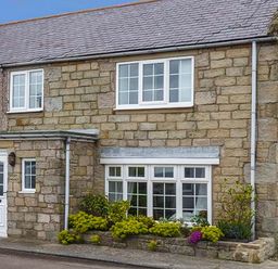 Stone house with white framed windows and a white door with plants in front at Sandy Knowes in Low Hauxley near Amble