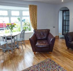 A sitting room with a round table and two chairs by a window and two brown armchairs at Sandy Knowes in Low Hauxley near Amble