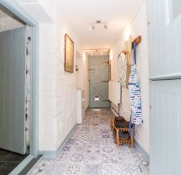 A narrow hallway with patterned tile floor blue doors hooks on the wall and a wooden shoe rack at The Old Dairy Maker near Millbrook