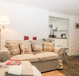 A living room with a beige sofa and pillows next to a floor lamp and a small white table with cups in a home with stone walls at The Old Dairy Maker near Millbrook