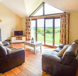 A living room with two black leather sofas a coffee table and a TV near large windows at Black Mountain View in Llanafan Fawr near Builth Wells