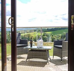 A balcony with wicker chairs and a table set with wine glasses and a lantern overlooking green fields at Black Mountain View in Llanafan Fawr near Builth Wells