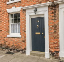 A brick building facade with a black door numbered 24 a window with white curtains and a yellow door at 24 College Lane Stratford-Upon-Avon
