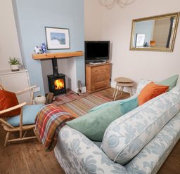 A living room with a wood stove fireplace a chair a patterned sofa with cushions a wooden chest of drawers and a large wall mirror at 24 College Lane in Stratford-Upon-Avon