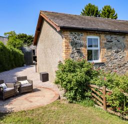 An outdoor seating area with chairs and a table near a stone wall at Peniarth in Penybontfawr near Oswestry