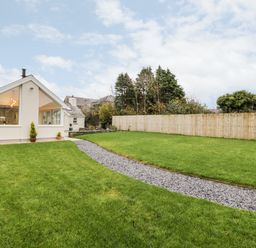A backyard with green grass gravel path wooden fence and part of a house with large windows at Ty'n Lon Bach in Llandwrog