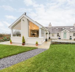 A house with a glass extension and green lawn in the foreground at Ty'n Lon Bach in Llandwrog