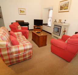 A living room with red and plaid sofas a wooden coffee table a TV on a wooden stand and a fireplace at Kingfisher Barn in Staveley near Windermere