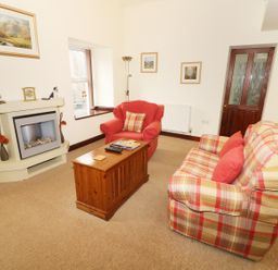 A living room with a plaid sofa and red armchair near a wooden chest and fireplace at Kingfisher Barn in Staveley near Windermere