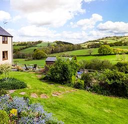 A garden with flowers and shrubs next to a house overlooking green fields and hills at Glebe Farm Cottage in Llandegveth near Cwmbran
