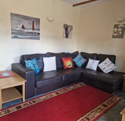 A living room with a black sectional sofa with multiple decorated cushions and wooden side tables at Kingfisher Cottage in Llanboidy