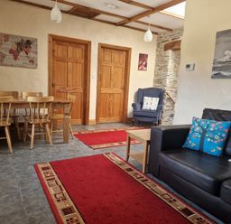 A living room with a black sofa with cushions a wooden dining table with chairs two wooden doors and a blue armchair at Kingfisher Cottage in Llanboidy