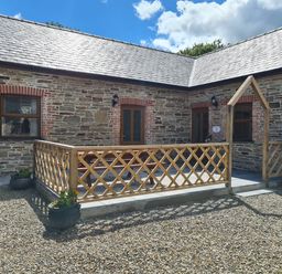 An outdoor patio with wooden railing and stone walls under a blue sky at Swallow Cottage in Llanboidy