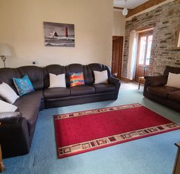 A living room with two brown leather sofas a red rug and a stone wall at Swallow Cottage in Llanboidy