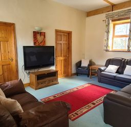 A living room with brown leather sofas a red rug a wooden TV stand a flat screen TV and two wooden doors at Swallow Cottage in Llanboidy