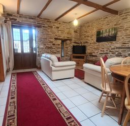 A living room with stone walls wooden beams white tile floor white sofas wooden dining table and chairs at Sandpiper Cottage in Llanboidy