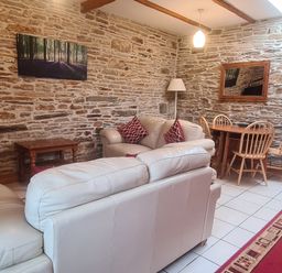 A living room with cream sofas red cushions a wooden dining table and chairs with stone walls at Sandpiper Cottage in Llanboidy