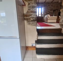 Stone steps leading to a living room with a red rug beige sofa and wooden door next to a white fridge in a stone wall house at Sandpiper Cottage in Llanboidy