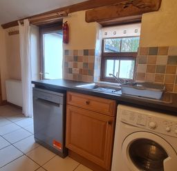 A kitchen with dishwasher washing machine sink and wooden cabinets at Sandpiper Cottage in Llanboidy