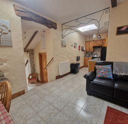 A tiled floor room with a black couch and kitchen area in the background at Puffin Cottage in Llanboidy