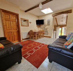 A sitting room with two black sofas a red rug a wooden dining table with chairs and a wall mounted TV at Puffin Cottage in Llanboidy