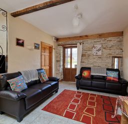 A living room with two black sofas with colorful cushions a red patterned rug and a wooden door at Puffin Cottage in Llanboidy