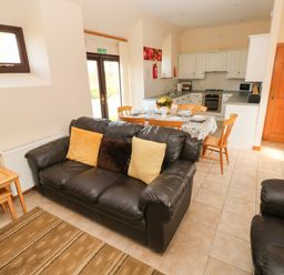 A living area with black sofas and a dining table set with chairs near a kitchen with white cabinets at Hill Top Farm Cottage Martletwy near Narbeth