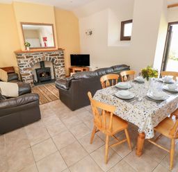 A living room with leather sofas a stone fireplace a television and a dining table set for six at Hill Top Farm Cottage in Martletwy near Narbeth