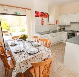 A kitchen with white cabinets a dining table set with plates glasses and cutlery and a fire exit door at Hill Top Farm Cottage Martletwy near Narbeth