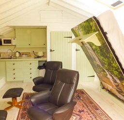 A small kitchen area with light green cabinets and black chairs with a fold-up bed in a white paneled room at Beech View in Malton
