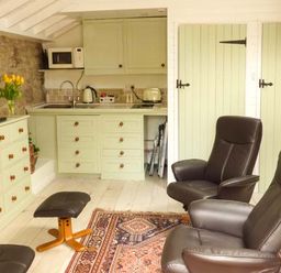 A small kitchen with cabinets a microwave a kettle and a toaster two leather armchairs a matching footstool a dresser with a television and a vase of flowers at Beech View in Malton