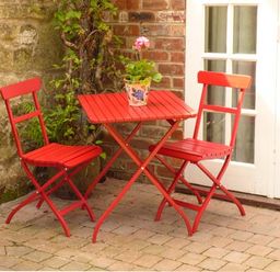 A red table with two red chairs and a potted plant on the table on a brick patio at Beech View in Malton