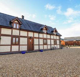 A gravel courtyard in front of a timber framed building with dormer windows and a wooden door at The Old House in Llanidloes