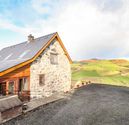 Stone and wood house with gravel driveway and green hills in the background at The Old House in Llanidloes