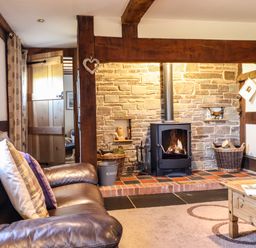A living room with a leather sofa and pillows a stone fireplace with a wood stove and a wooden coffee table at The Old House in Llanidloes