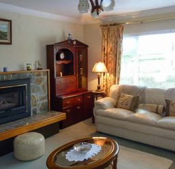 A living room with a stone fireplace a leather sofa cushions a wooden cabinet a lamp and a window with curtains at Eileen's in Aughavas near Mohill County Leitrim