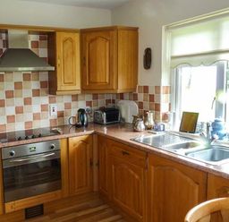 A kitchen with wooden cabinets a sink an oven a kettle a toaster and a window at Eileen's in Aughavas near Mohill County Leitrim