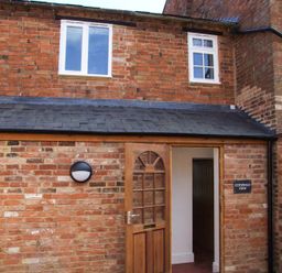 A brick exterior wall with a wooden door open and two windows above at Cotswold View in Clifford Chambers near Stratford-upon-Avon