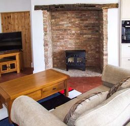 A living room with a beige sofa a wooden coffee table a TV on wooden stand a brick fireplace and a built-in oven at Cotswold View in Clifford Chambers near Stratford-upon-Avon