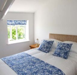 A bedroom with a bed with blue and white cushions and runner near a window with a blue patterned blind at Cotswold View in Clifford Chambers near Stratford-upon-Avon