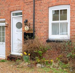 The entrance of a brick house with white doors and windows and plants in front at 5 Melinda Cottages in East Runton near Cromer