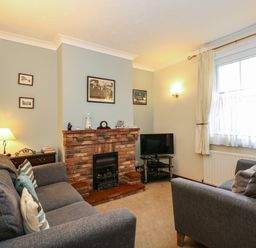 A living room with two gray sofas a brick fireplace a small television on a stand and a window with curtains at 5 Melinda Cottages in East Runton near Cromer