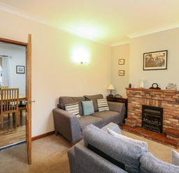 A living room with two grey sofas a brick fireplace and a wooden dining table visible through an open door at 5 Melinda Cottages in East Runton near Cromer